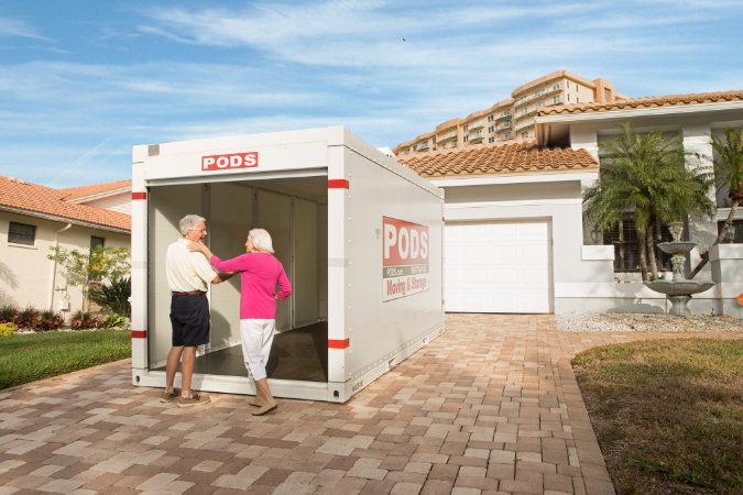A happy senior couple is standing beside an empty PODS container in the driveway of their new home in Pensacola.