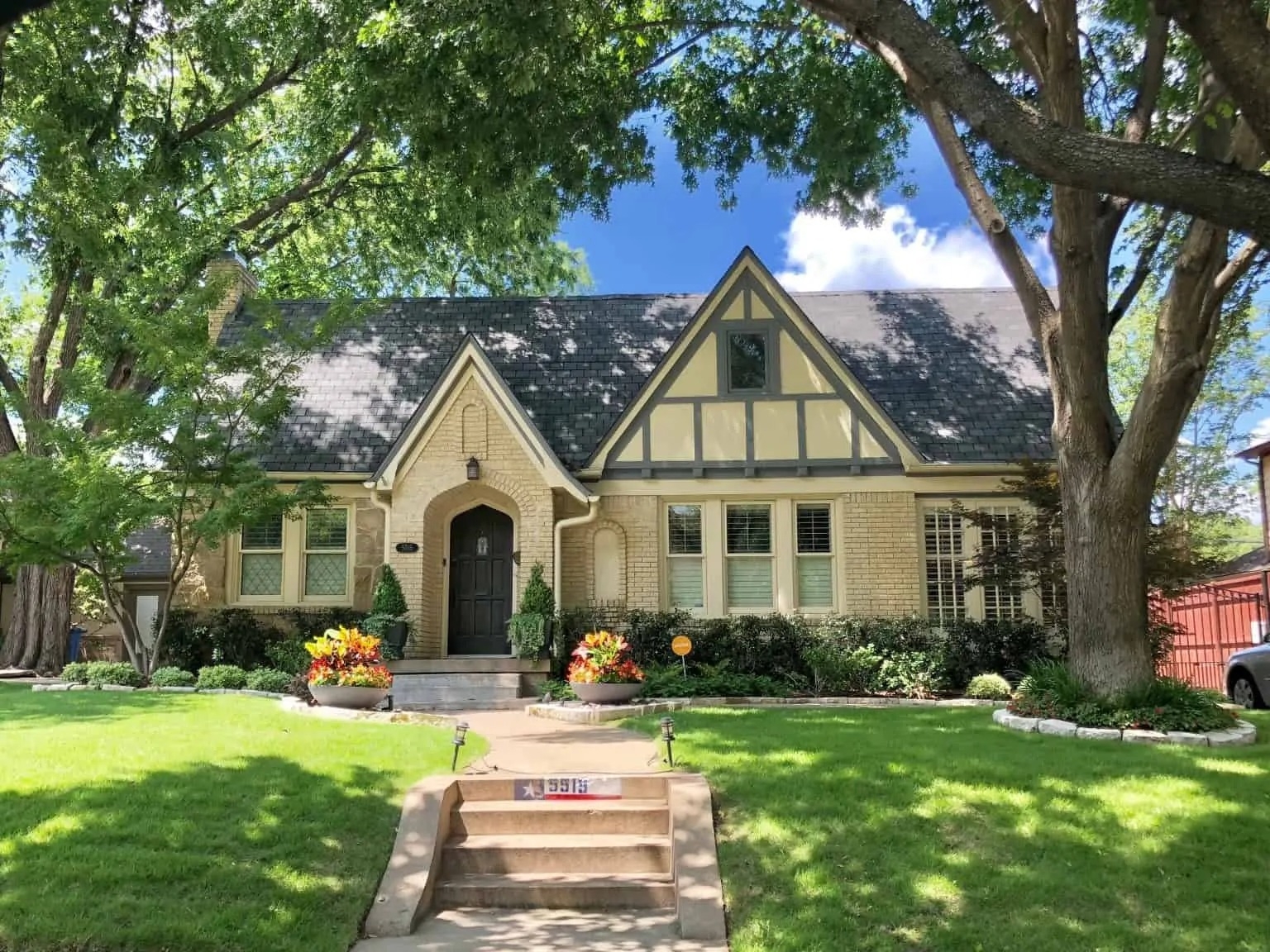 A yellow multi-story mansion in the neighborhood of Greenland Hills in Dallas, Texas. There are steps that lead up to the home, and there are plants on either side of the stairs. 