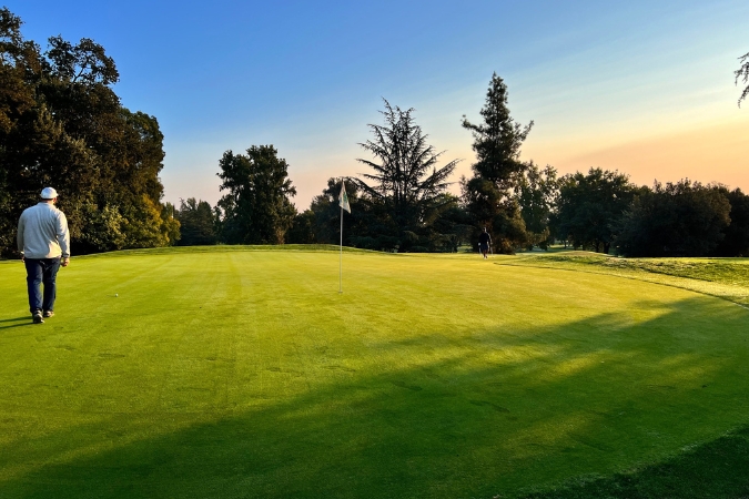 A local enjoys a sunset round at Ancil Hoffman Golf Course  — one of many fun things to do in Sacramento — surrounded by lush trees and greenery.