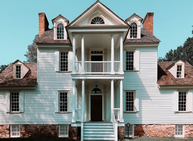 A stately mansion in the Myers Park area of Charlotte, NC. The home has white siding, a brown roof, a large front porch staircase, and a second-floor balcony.