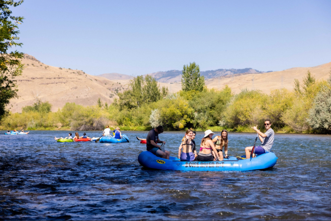 Group of people floating on blue inflatable rafts along a calm river in Boise, Idaho, on a sunny day — one of the major pros on the list of pros and cons of living in Boise, Idaho.
