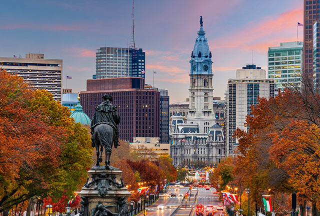 A view of downtown Philadelphia. It’s sunset, and traffic in the foreground is light. There are city buildings in the background.