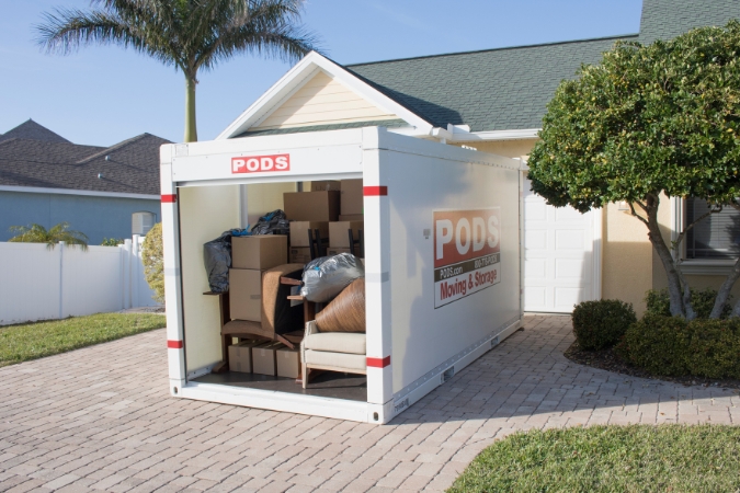 A PODS portable moving container, filled with moving boxes and furniture, is positioned in a residential driveway during a move.