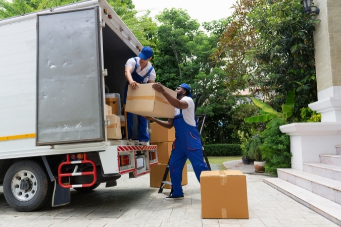 Two men pass a moving box between them while loading a moving truck during a summer move.