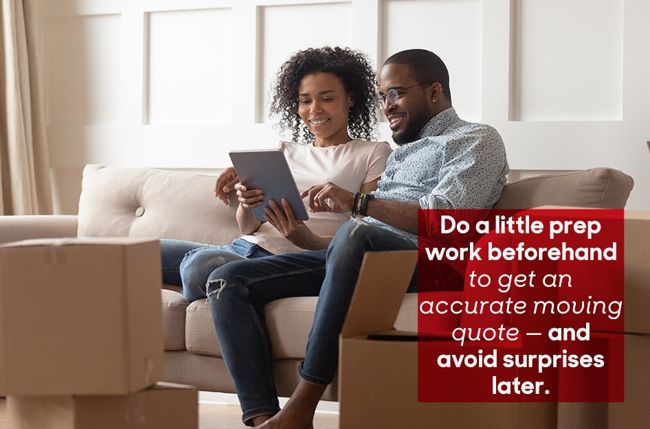 A young couple sits on their sofa and gets moving quotes online using their tablet. There are multiple moving boxes nearby. The overlay text reads “Do a little prep work beforehand to get an accurate moving quote — and avoid surprises later.”