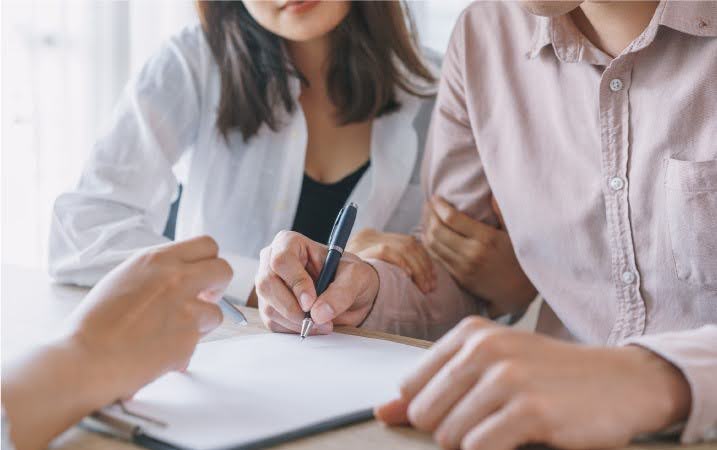 After finding an apartment in Los Angeles, a couple reviews the rental agreement for their new place as the landlord uses a pen to show them where to sign.
