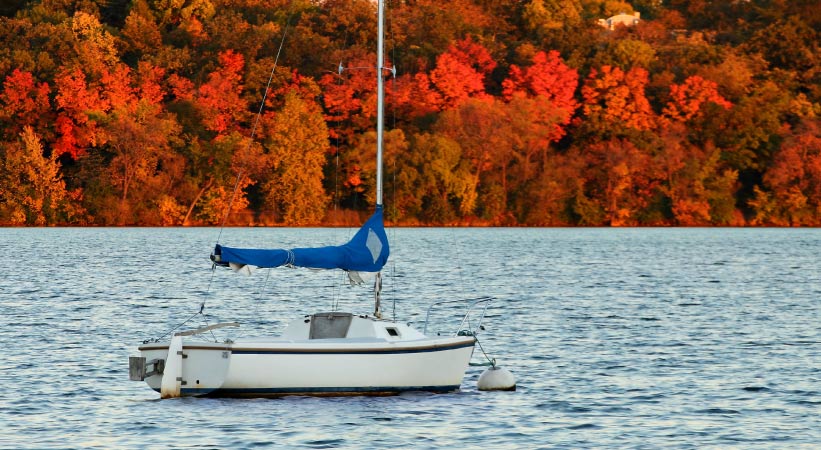 A sailboat on Lake Harriet in Minneapolis during autumn. The trees on the shoreline are a striking rainbow of oranges, reds, and yellows