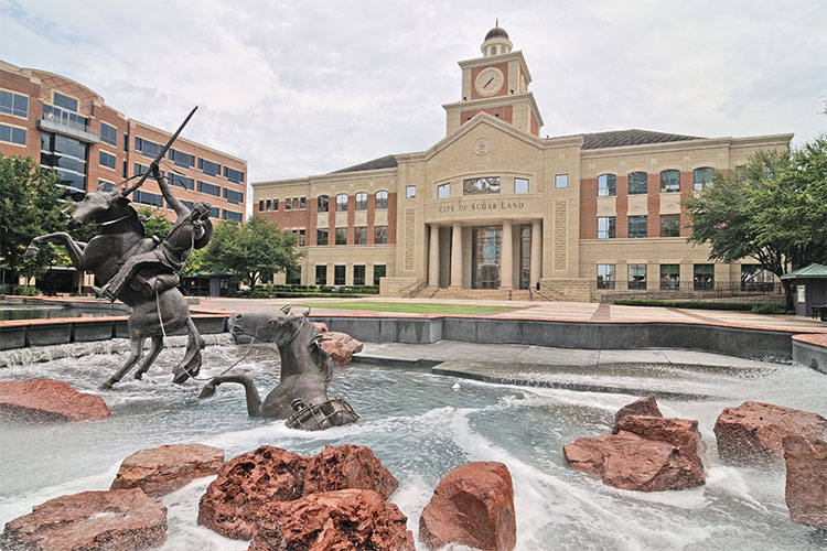 The Sugar Land Town Square, featuring an impressive city building and a water feature with sculptures of horses and a rider. 