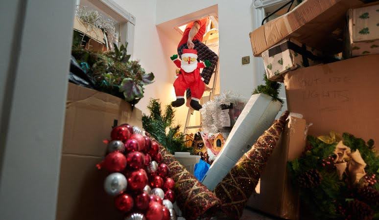 A man carrying boxes of Christmas decorations into the attic where he’s designated a Christmas decoration storage space.