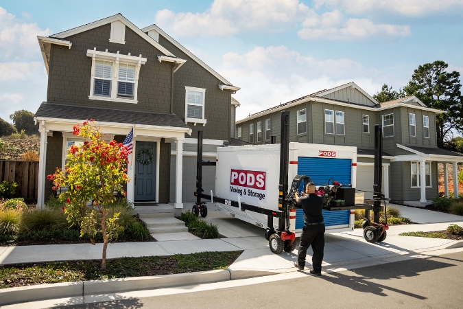 A PODS driver is using PODZILLA to position a portable storage container in a residential driveway.
