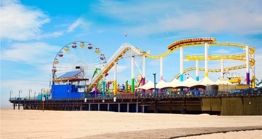 View of the colorful roller coaster and ferris wheel on Santa Monica Pier on a sunny day in Santa Monica, California.