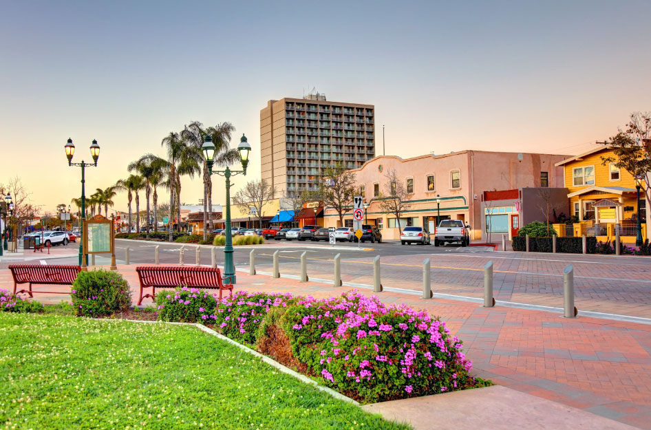 Downtown Chula Vista, California, at sunrise. There are park benches and cars parked at local businesses.