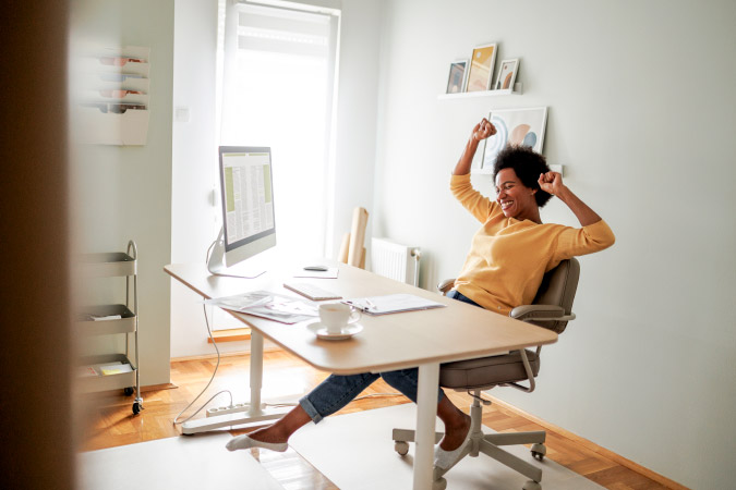 A happy woman is smiling and celebrating at her desk — a new addition to her home office setup.