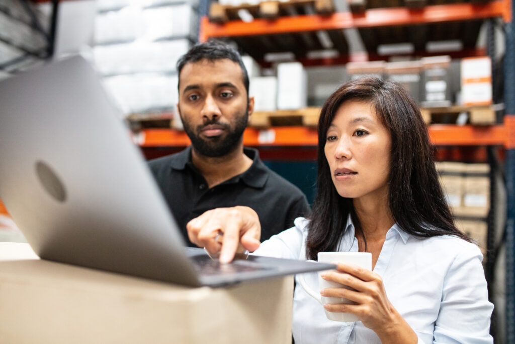 Female and male employee using a laptop inside a warehouse