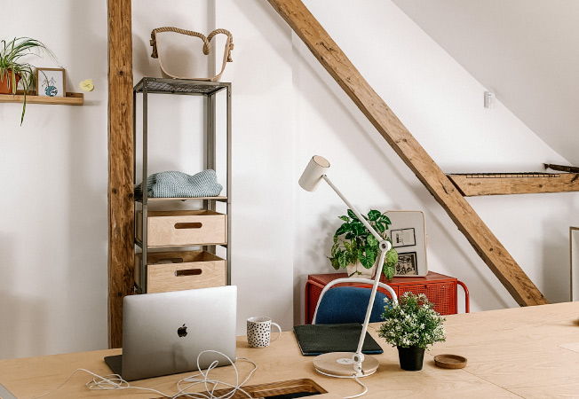 An attic that’s been renovated into a home office. The natural wood rafters are left exposed against finished white walls. 