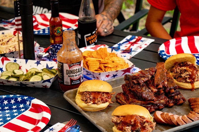 Outdoor table showcasing barbecue favorites such as pulled pork sandwiches, ribs and sausage at Dinosaur Bar-B-Que, a must-try restaurant when living in Rochester, NY.