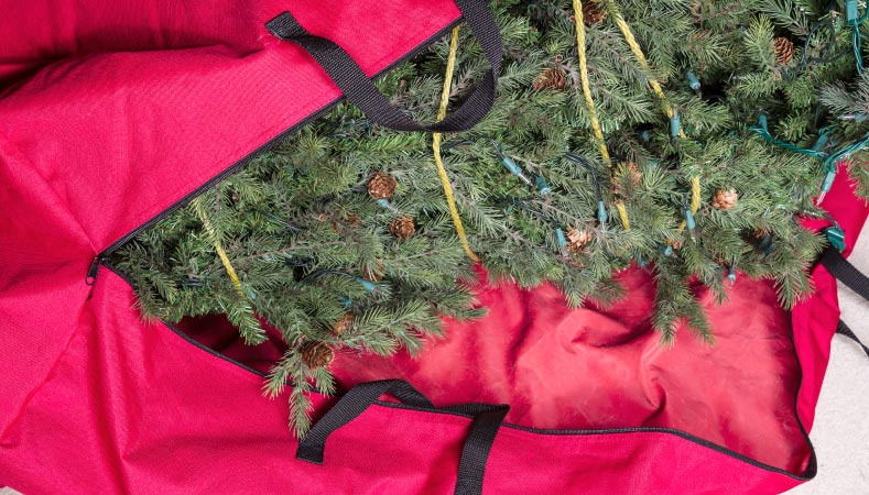 An artificial Christmas tree in a red Christmas tree storage bag.