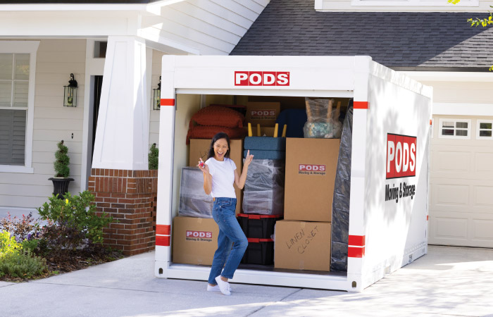 A woman strikes a happy pose in front of her loaded PODS portable moving container.