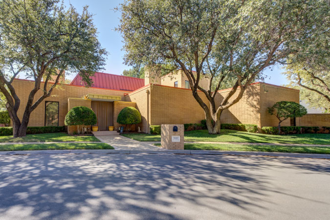 A four-bedroom modern home in LakeRidge — one of the best Lubbock neighborhoods — featuring a yellow brick exterior and red tin roof.