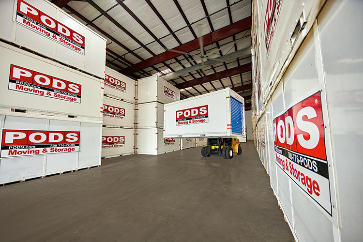 A forklift driver is placing a PODS moving and storage container on top of another one in a secure storage facility. There are several other PODS containers stacked neatly around these.