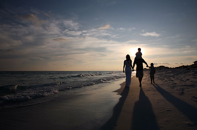 A family walking together on the beach, silhouetted by the setting sun