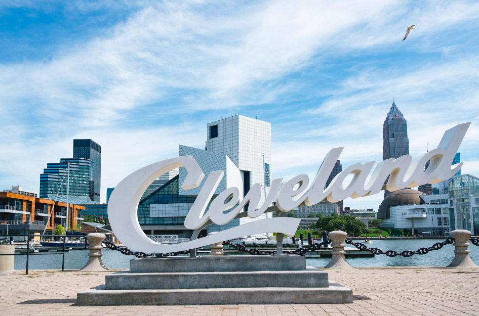 A stylized “Cleveland” sculpture in Cleveland, Ohio, with the city skyline visible in the background on a sunny day.