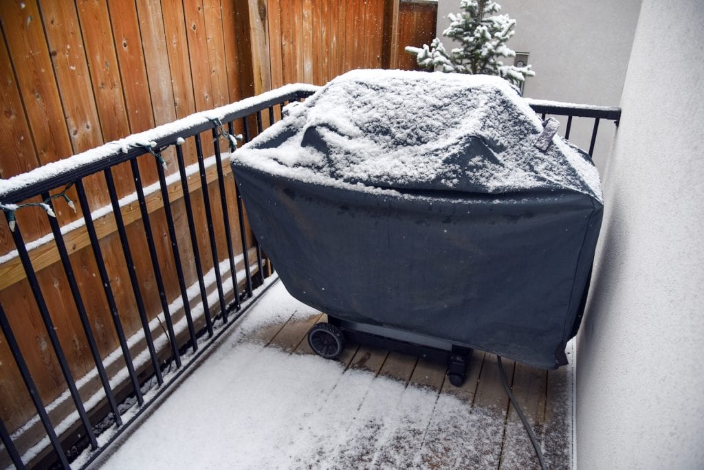 A gas grill covered with canvas as well as a dusting of fresh snow as it sits exposed on a patio instead of safe in winter storage.