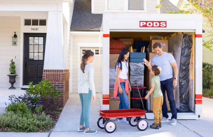 A family of four has a lively conversation at the front of their PODS portable moving container, which is almost fully loaded.