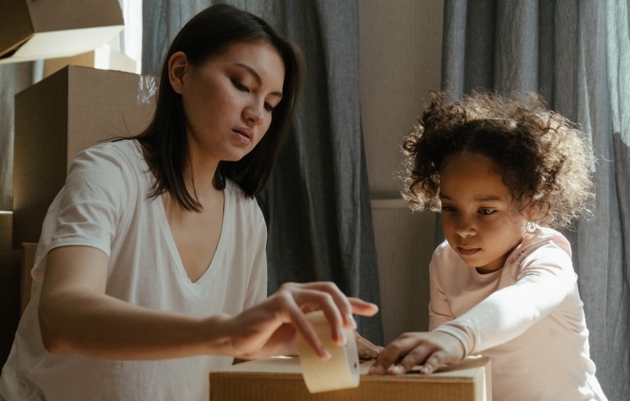 A woman and her young child are packing up moving boxes in accordance with their moving checklist (apartment-version).