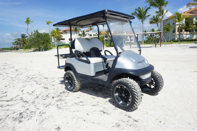 A golf cart sits on a white sand beach.