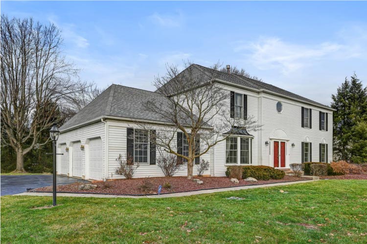 A split-level house in Princeton Junction, New Jersey, features a white siding exterior, black shutters, and a red front door. 