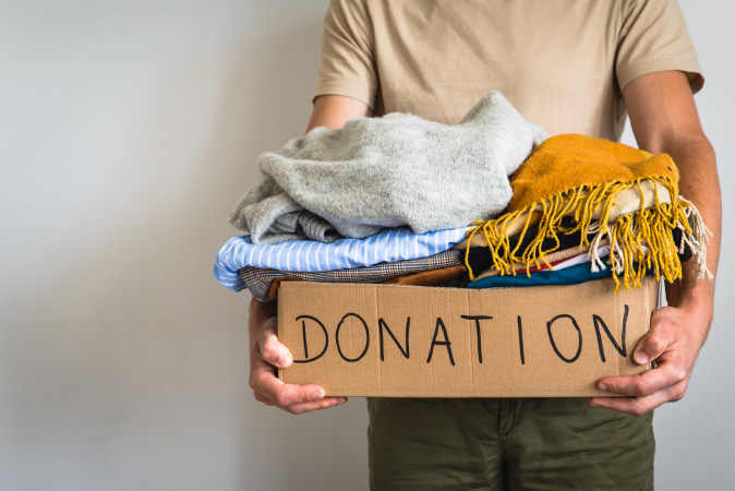 After learning how to downsize, a man is holding a box labeled “DONATION” that is filled with miscellaneous clothing items.