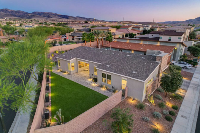 Elevated view of a one-story home in Inspirada — one of the best neighborhoods in Henderson, NV — featuring a green backyard with a stone wall for privacy.