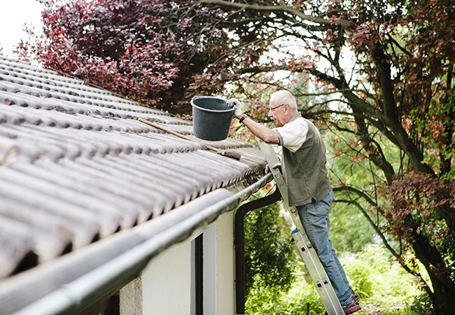 A gentleman clears the gutters of his home