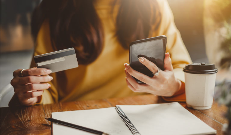 A woman paying bills on her phone in a cafe