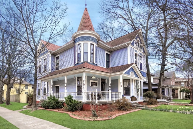 Powder blue Queen Anne Victorian-style home in Downtown Little Rock, Arkansas, with a manicured lawn and tall trees that have shed their leaves.