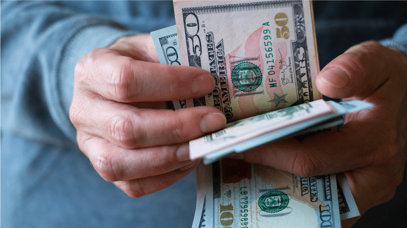  A pair of hands is counting out large U.S. bills, including a few fifty- and hundred-dollar bills.