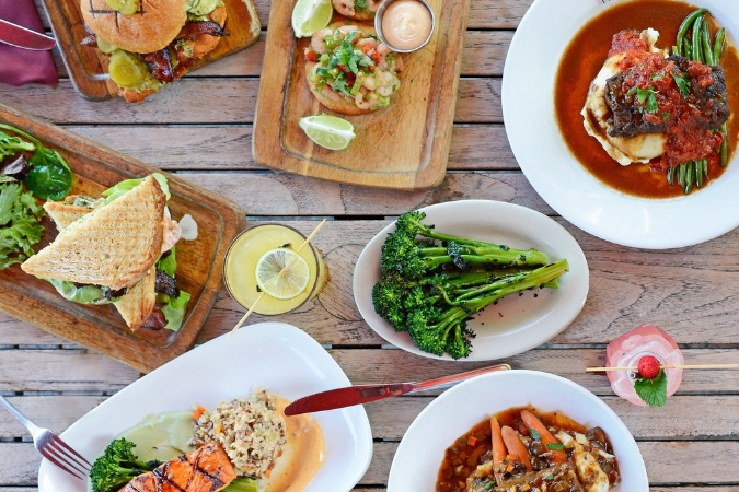 View from above of a table set with assorted dishes from Dada — one of the many restaurants in Delray Beach — including a salmon plate, broccoli, braised short rib, club sandwich, drinks and more.