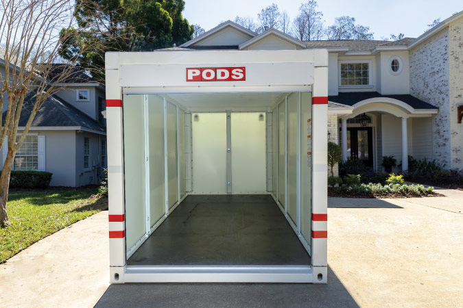 Head-on view of an empty PODS portable storage container with its door open, sitting in a residential driveway.