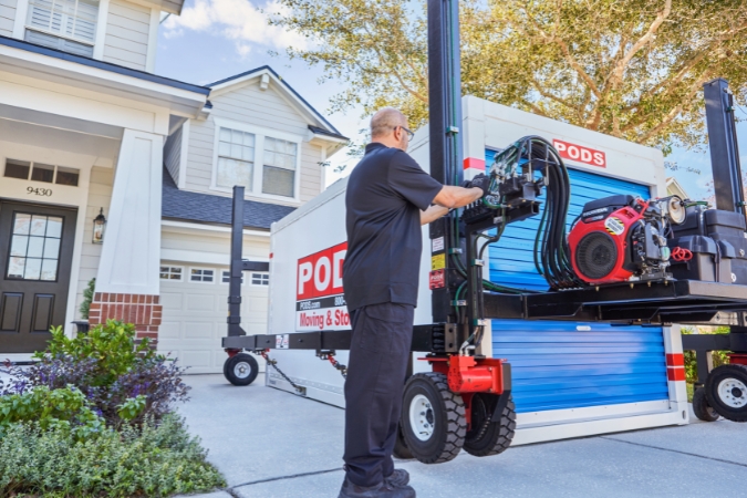 A PODS driver lowers a portable moving container into the driveway of a family's new home after they relocated using PODS rather than full-service movers.