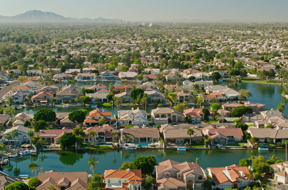 Aerial view of a residential area in the city of Gilbert, Arizona. There’s an artificial lake with rows of waterfront homes, and trees dispersed throughout the area.