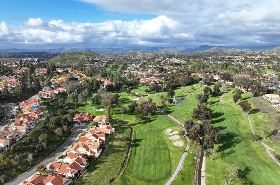 Aerial view of the beautiful Rancho Bernardo residential area in San Diego, featuring a pristine golf course in the foreground and mountains in the distance.