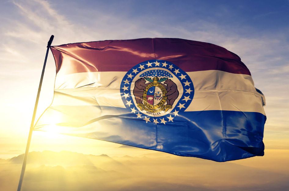 The Missouri state flag blowing in the wind at the top of a flagpole.