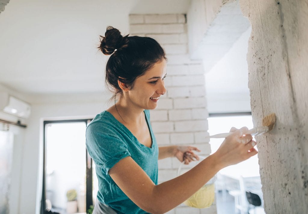 A young woman in a blue top paints columns in her home