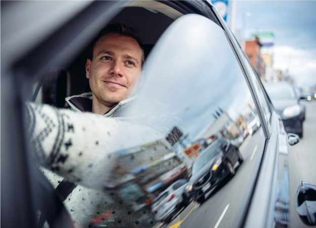 A man drives through Toronto as he smiles and admires the city through his car window.