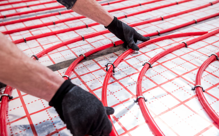Close-up of a contractor’s gloved hands as they install elements of heated primary bathroom flooring.