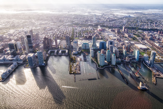 Afternoon light casts long shadows from the buildings of Jersey City on the Hudson River.