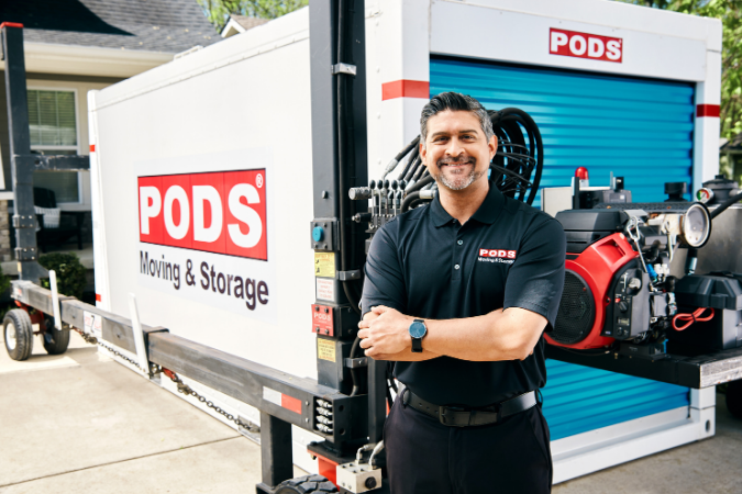 A truck driver stands nfornt of a PODS container and PODZILLA as someone gets ready to move furniture across the country.
