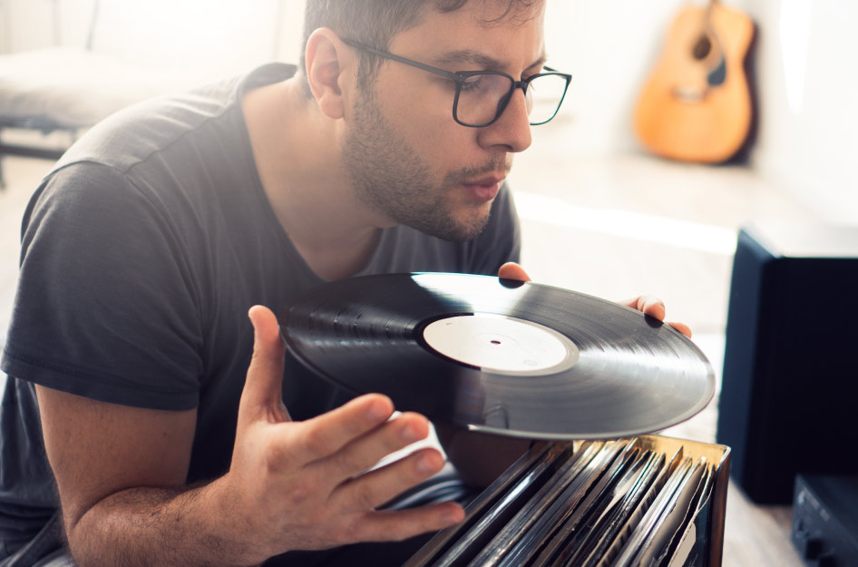 A man is holding a vinyl record and lightly blowing the dust off its surface before storing it away securely.