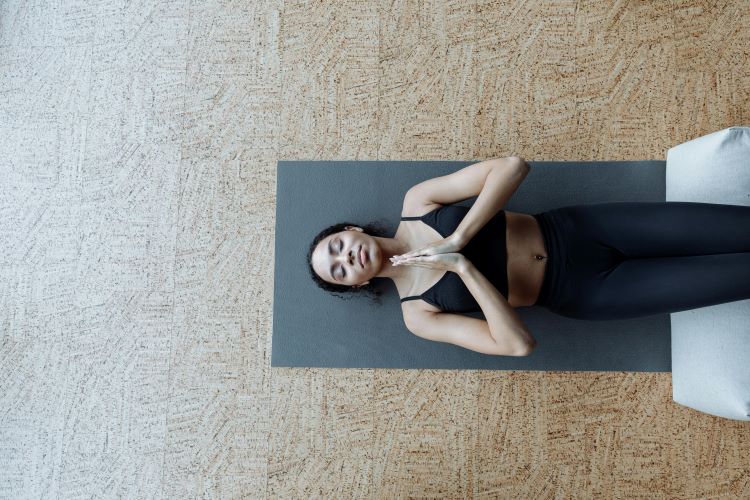 A womanlying on the ground with her hands folded as she practices the shavassana yoga position.